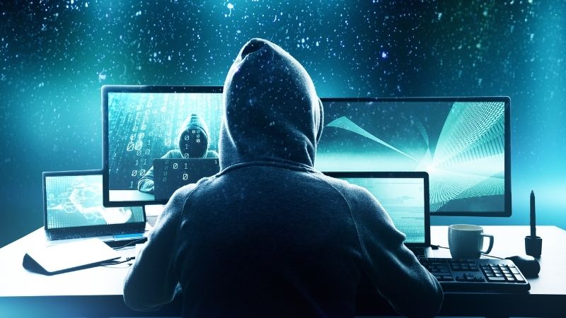 Figura encapuzada em frente a um notebook, sobreposta por ícones de e-mail e cadeado digital, representando um ataque de phishing com foco em interceptação de comunicações eletrônicas em escala global.