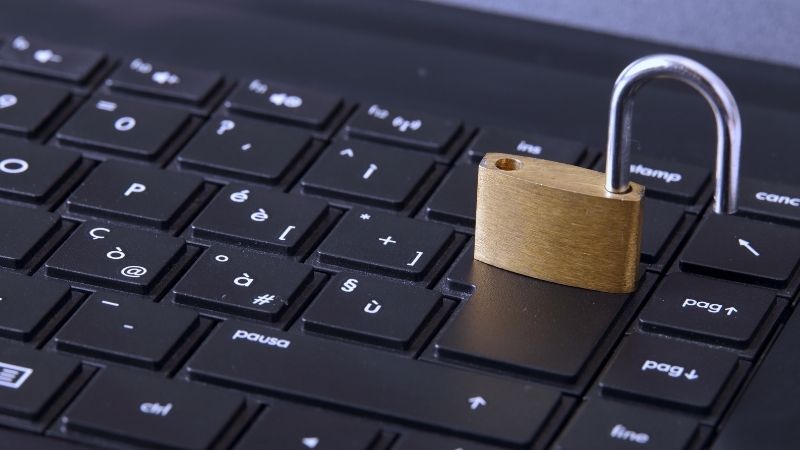 Um cadeado de metal repousa sobre o teclado de um laptop, simbolizando a segurança da informação. A foto destaca a importância de proteger os dados e os sistemas contra ataques de engenharia social.