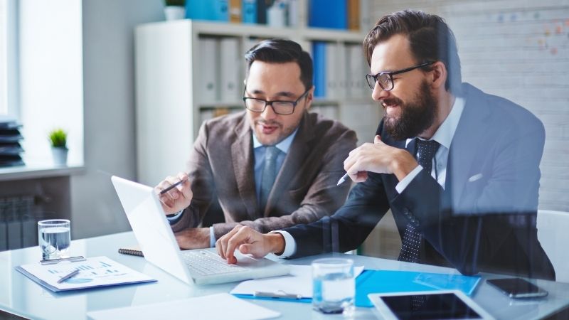 Dois profissionais de negócios analisando estratégias de segurança digital em um laptop, simbolizando o trabalho colaborativo em consultoria em cibersegurança.